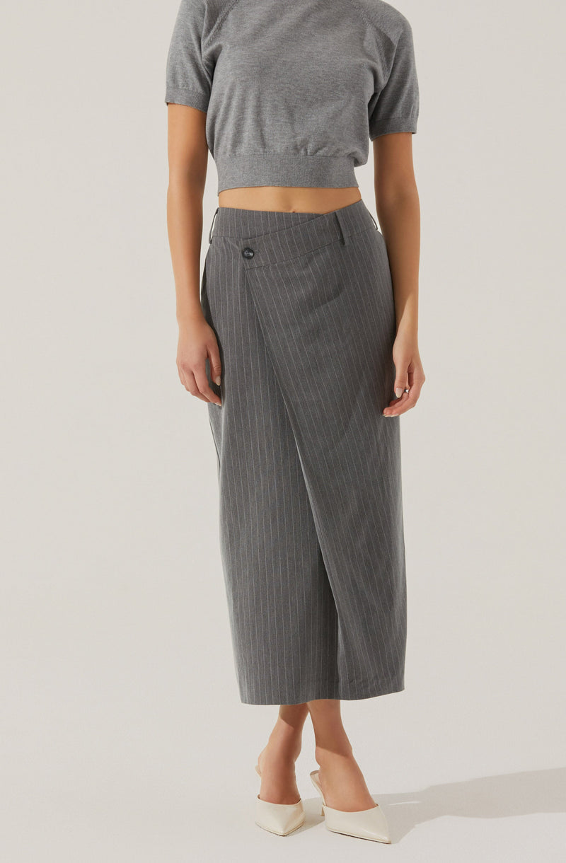 A person is wearing a loose-fitting, short-sleeved, grey crop top with a rounded neckline, paired with high-waisted, grey wide-leg trousers featuring thin vertical white pinstripes and a single button on the waistband. They are also wearing white pointed-toe high heels.