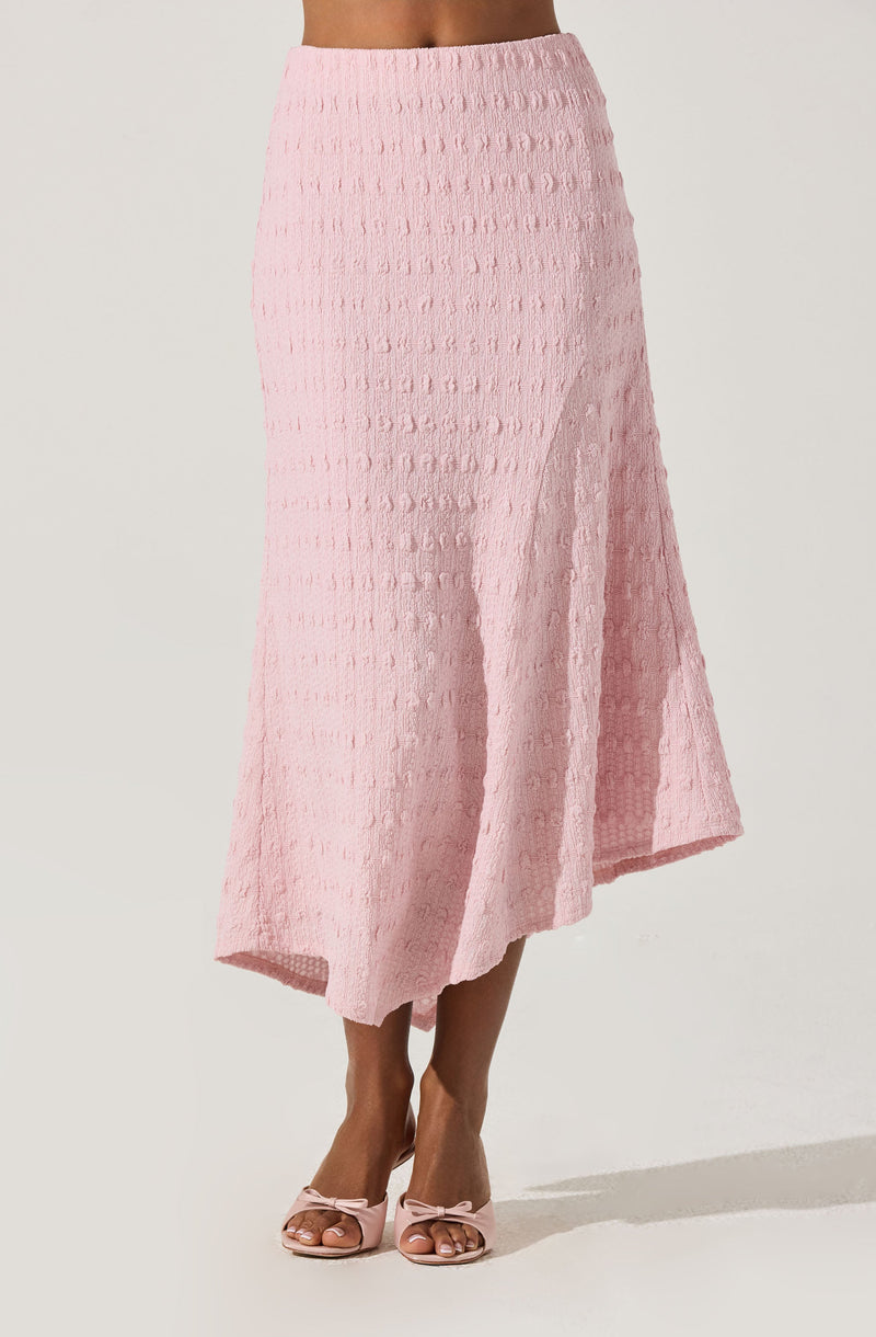 A woman is wearing a light pink, textured, mesh-like midi skirt that flares out slightly at the hem. She is also wearing pink high-heeled sandals with bows on the front.