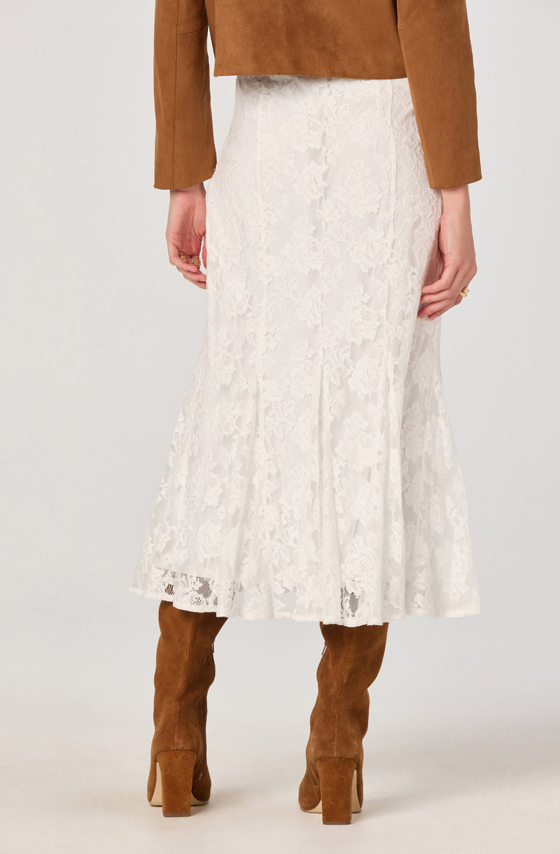 A person wearing a brown long-sleeve top, a white lace midi skirt with a ruffled hem, and brown knee-high suede boots with block heels.