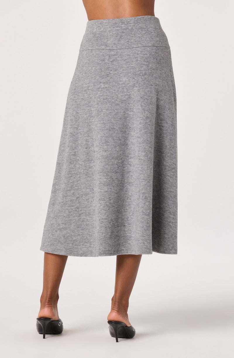 A woman is wearing a high-waisted, ankle-length gray skirt made of a soft, knit fabric. The skirt features a simple, clean design with a smooth waistband and no visible embellishments. She is also wearing black high-heeled shoes.