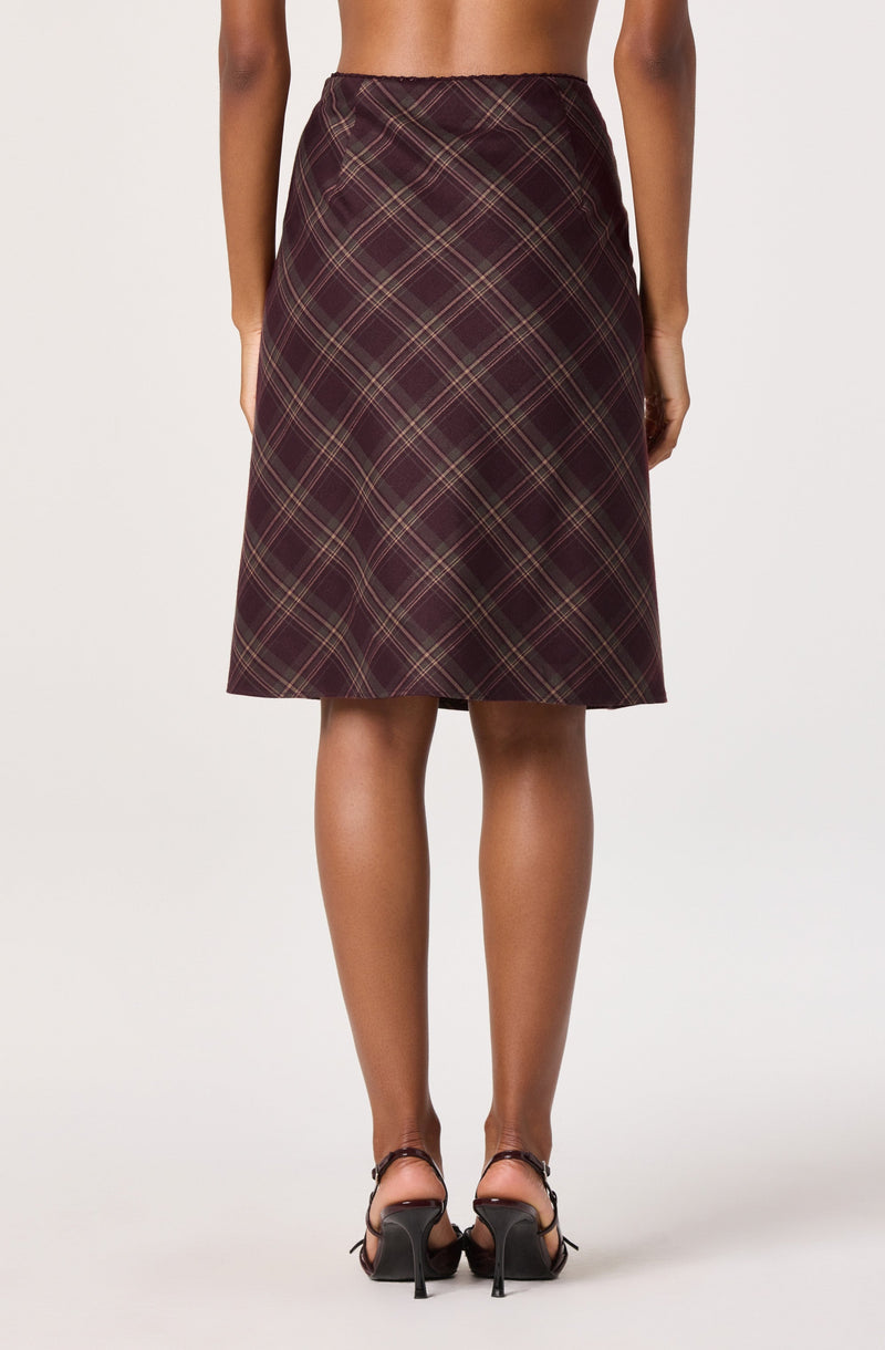 A woman is wearing a high-waisted, knee-length skirt with a plaid pattern in shades of dark red, black, and beige. She is also wearing black high-heeled shoes with ankle straps.