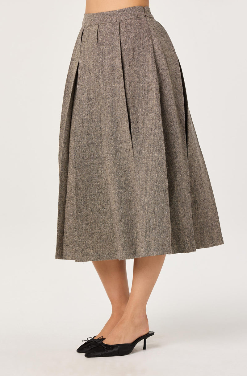 A person is wearing a high-waisted, ankle-length, brownish plaid skirt with pleats. The skirt has a subtle checkered pattern and appears to be made of a wool-like fabric. They are also wearing black pointed-toe kitten heels with a small bow on the front.