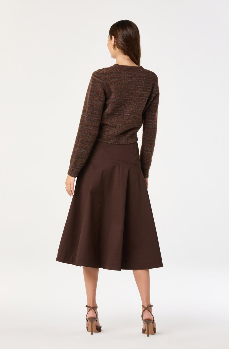 A woman is wearing a brown, textured, long-sleeve sweater paired with a high-waisted, full, midi-length skirt in a matching dark brown color. She is also wearing strappy, nude-colored high heels.