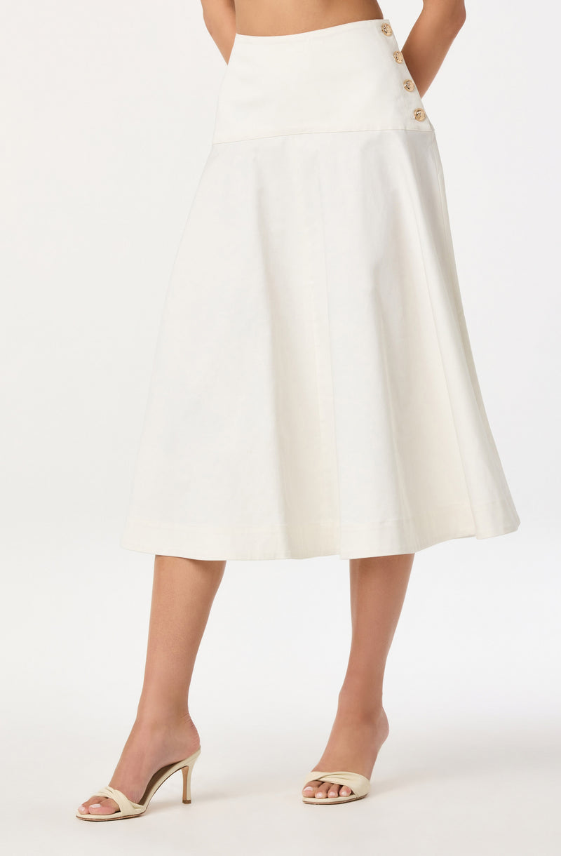 A woman is wearing a high-waisted, A-line midi skirt in a solid white color, featuring a row of four large, round buttons on the side near the waistband. She pairs the skirt with open-toe, mid-heel sandals in a neutral beige tone.