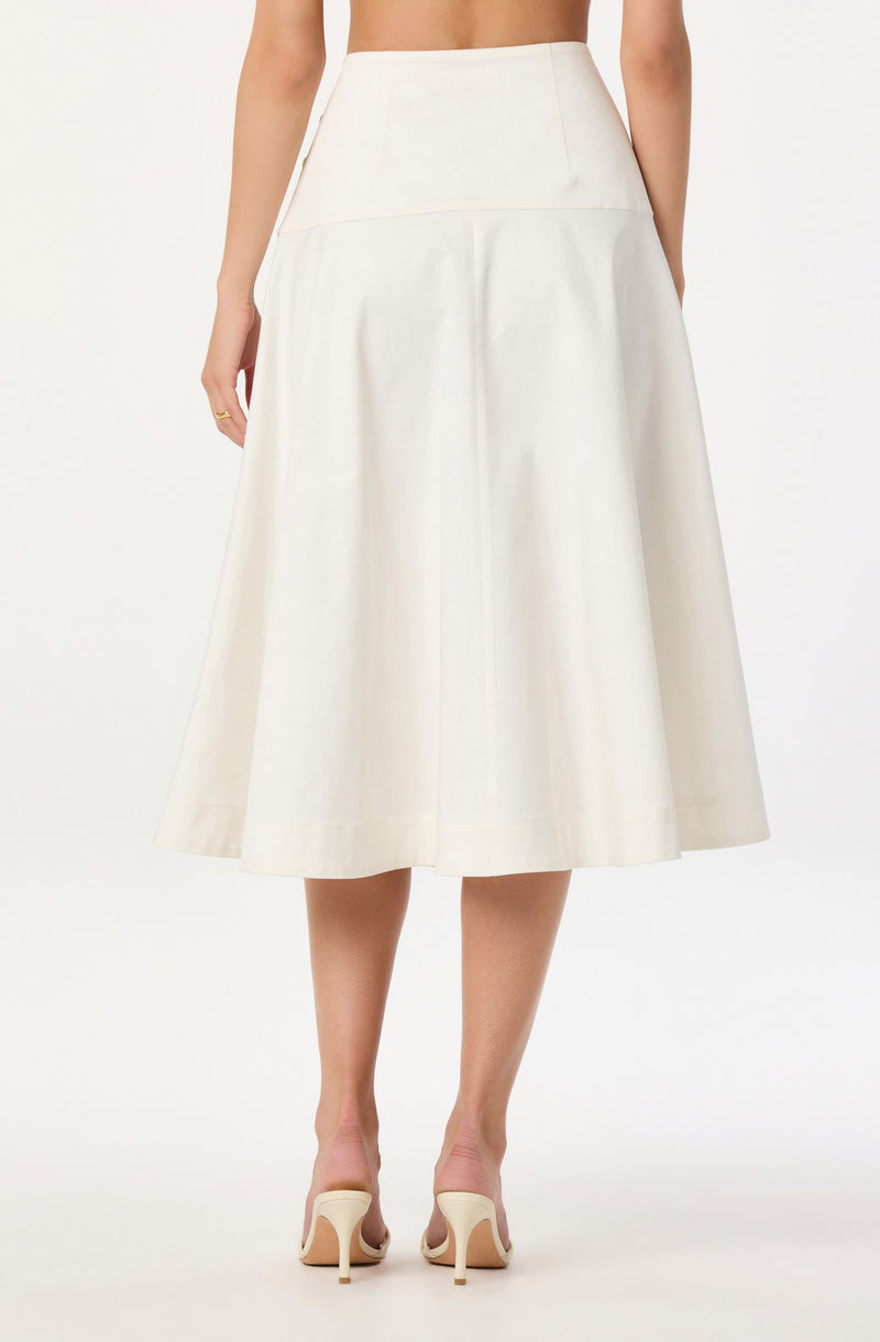 A woman is wearing a high-waisted, A-line midi skirt in an off-white color. The skirt has a smooth waistband and a full, flowing silhouette that reaches below the knees. She is also wearing a pair of beige high-heeled shoes.