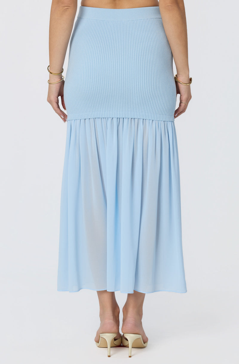 Light blue ribbed skirt with a ruffled, flowing hem, paired with beige heels.