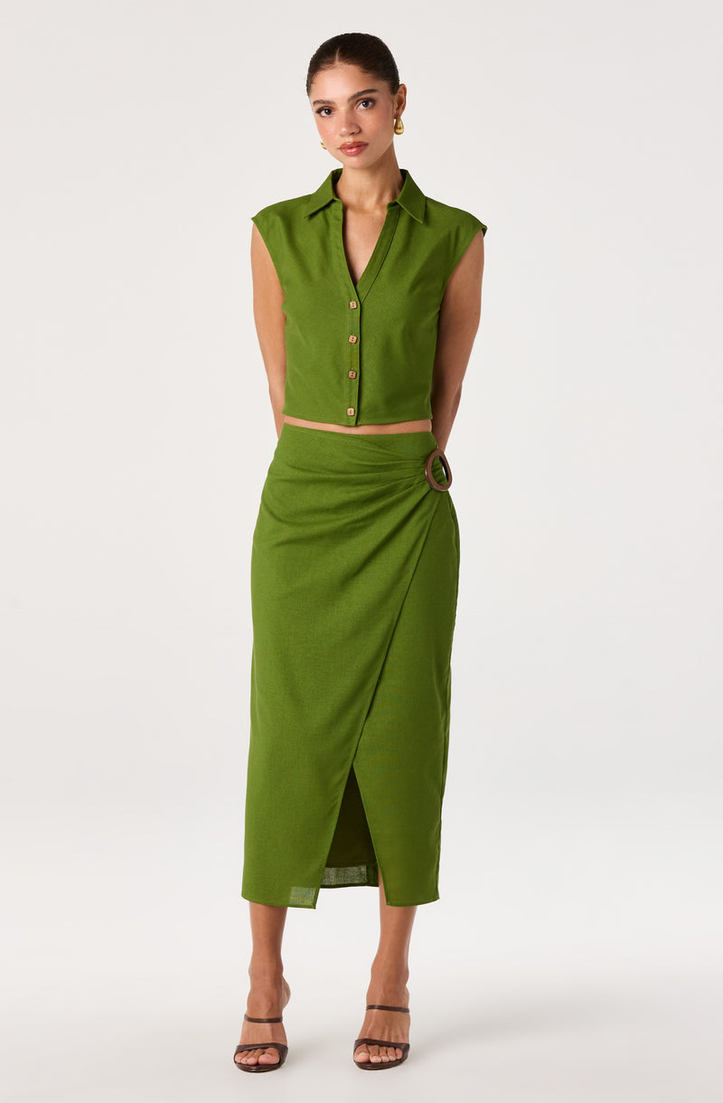 Woman wearing a sleeveless, collared, button-front green top and matching high-waisted skirt with a side slit and belt detail.