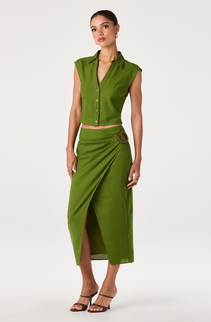 Woman in a sleeveless green shirt with a collar, and a matching green skirt with a ring detail and front slit.