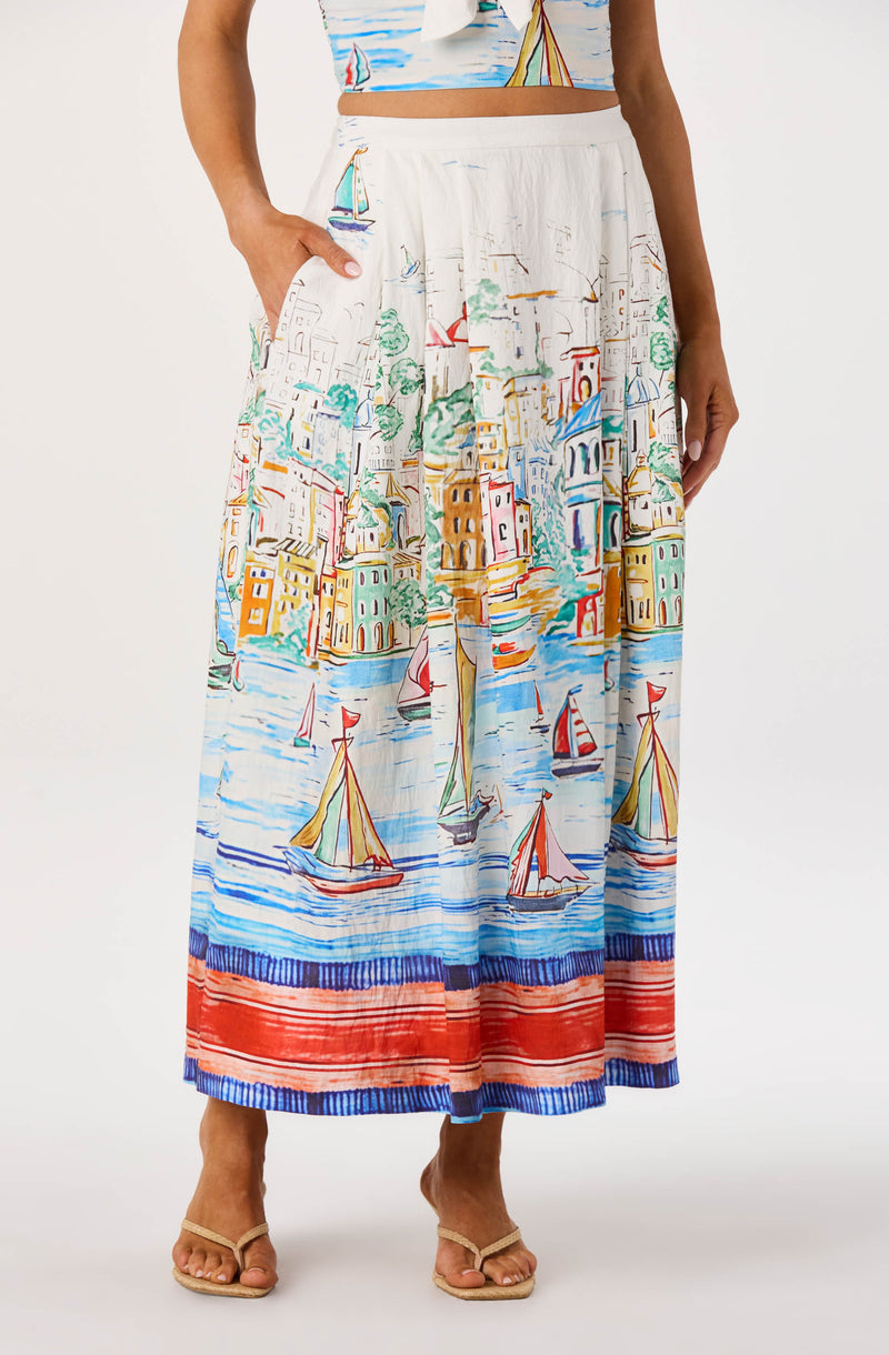 White skirt with colorful sailboats, buildings, and water scenes, high-waisted, flowy style.