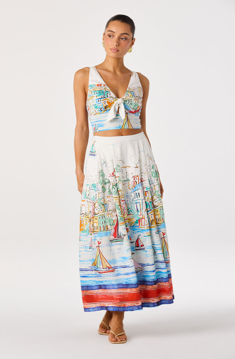 Woman wearing a colorful, printed sleeveless crop top and a matching wide-leg skirt with sailboat and cityscape design.