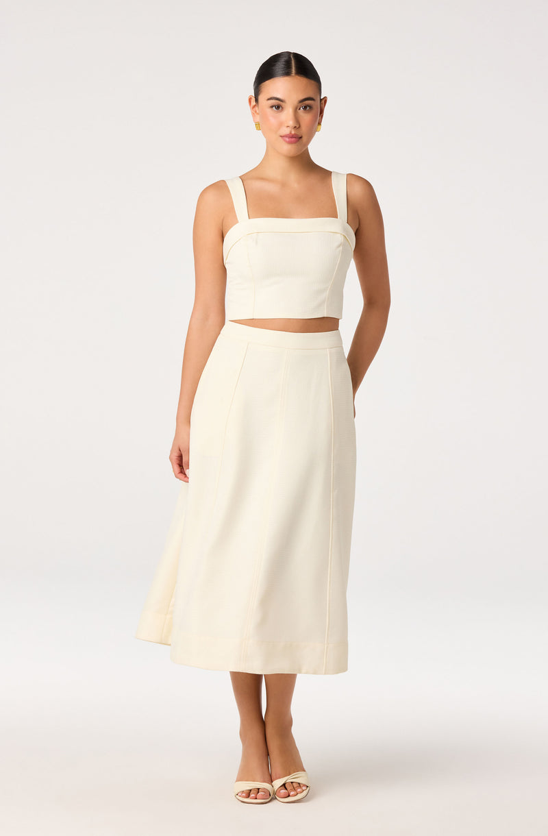 Woman wearing a cream crop top with wide straps and matching high-waisted midi skirt.