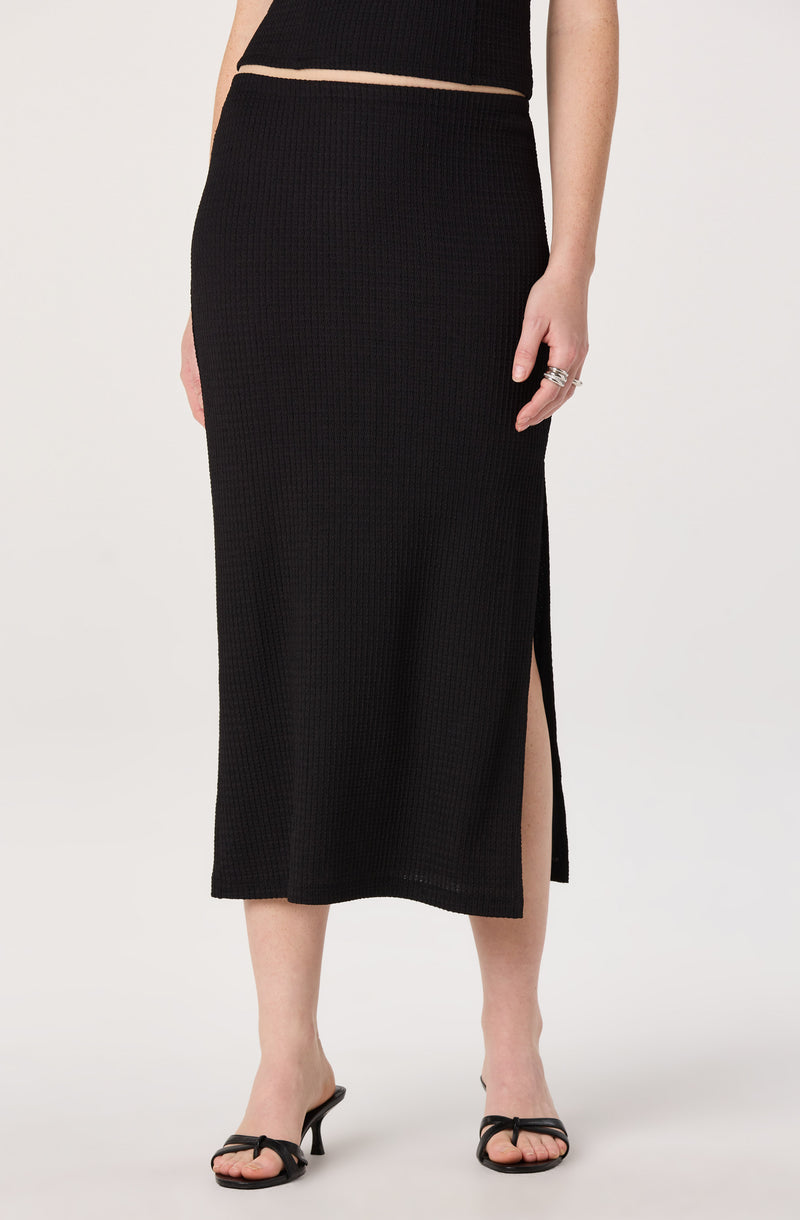 Black knit skirt with a side slit, paired with black open-toe heels.