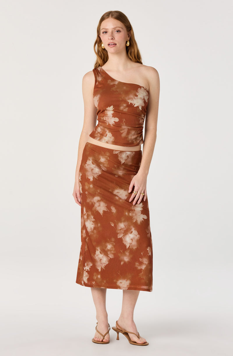 Woman wearing a brown tie-dye one-shoulder crop top and matching high-waisted skirt.