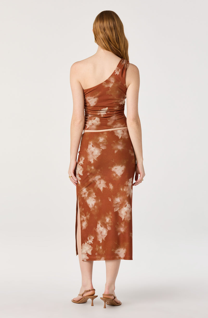 Woman in a brown tie-dye one-shoulder top and matching midi skirt with side slit.