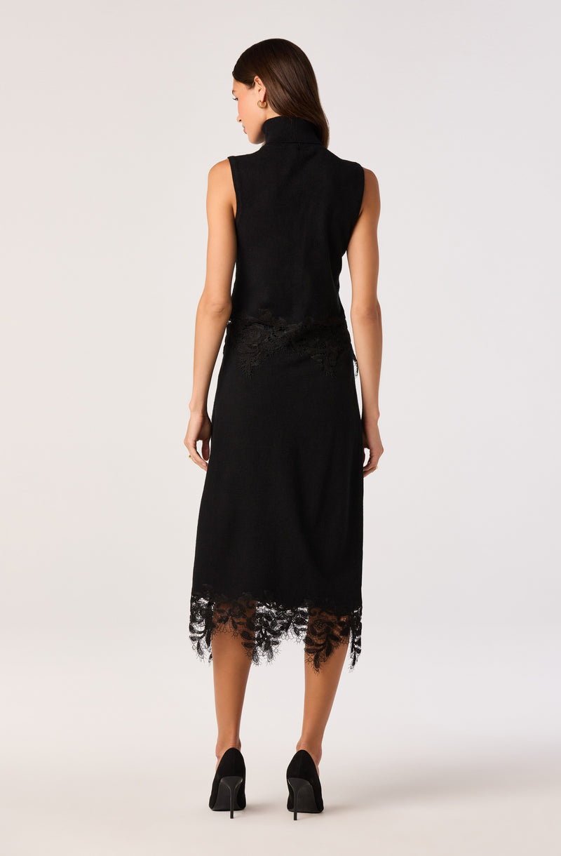 Woman wearing a sleeveless black dress with lace details at the hem and waist, paired with black high heels.