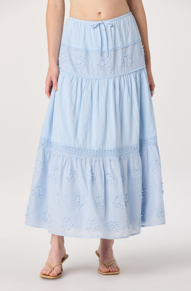 Light blue, tiered maxi skirt with embroidered and gathered details, paired with beige sandals.