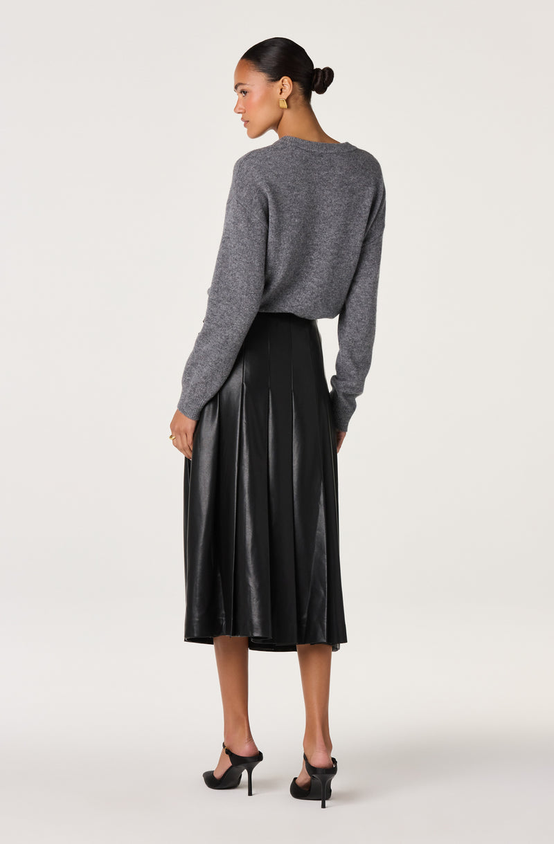 Woman wearing a gray fuzzy sweater, black leather pleated midi skirt, and black high heels.