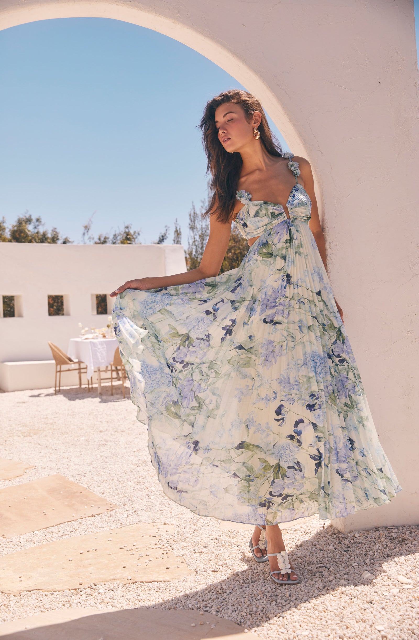 Woman in a sleeveless, floral maxi dress with ruffle straps, soft pastel colors.