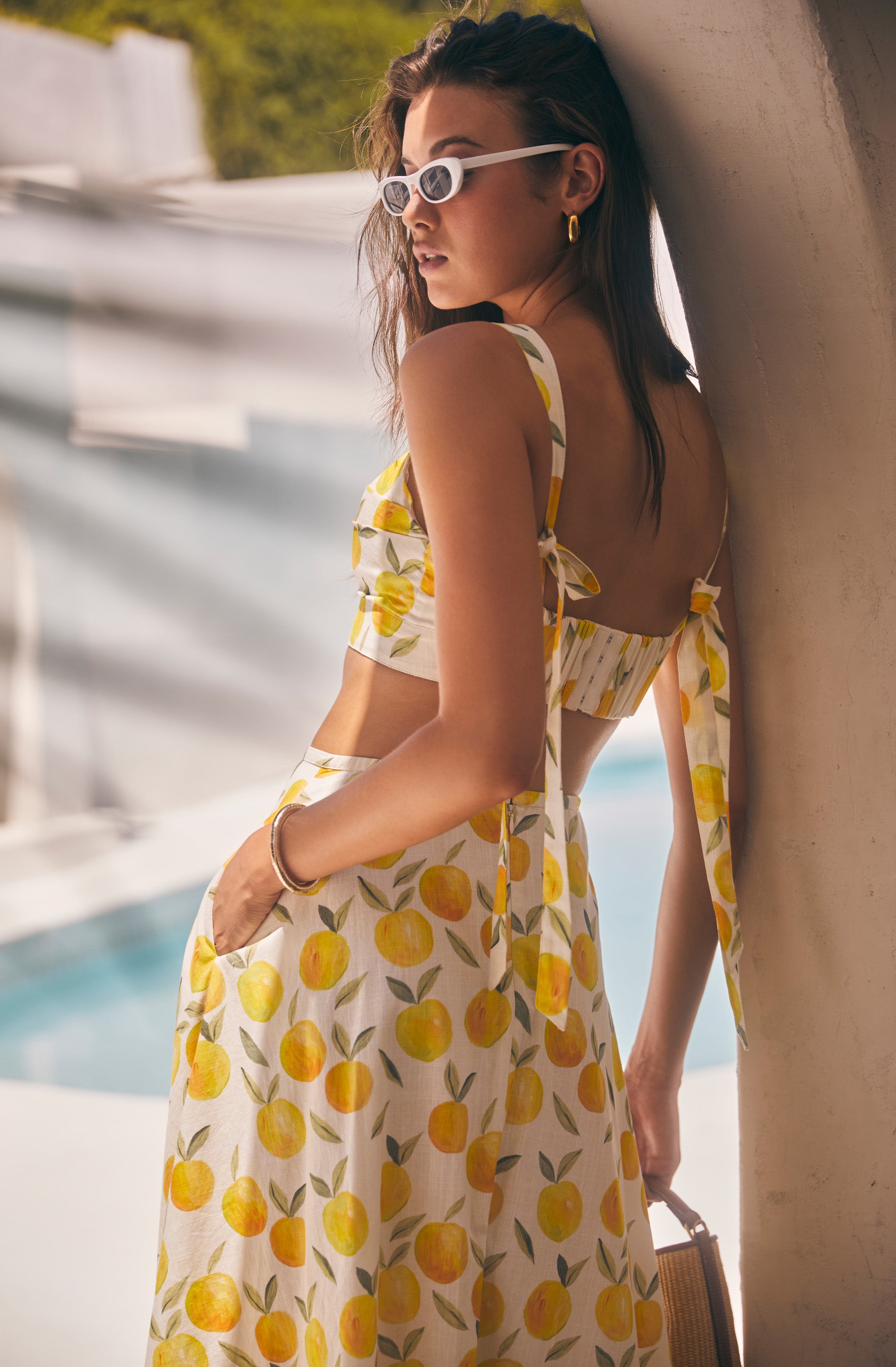 Woman in a lemon-printed matching top and skirt set, white sunglasses, and gold hoop earrings.