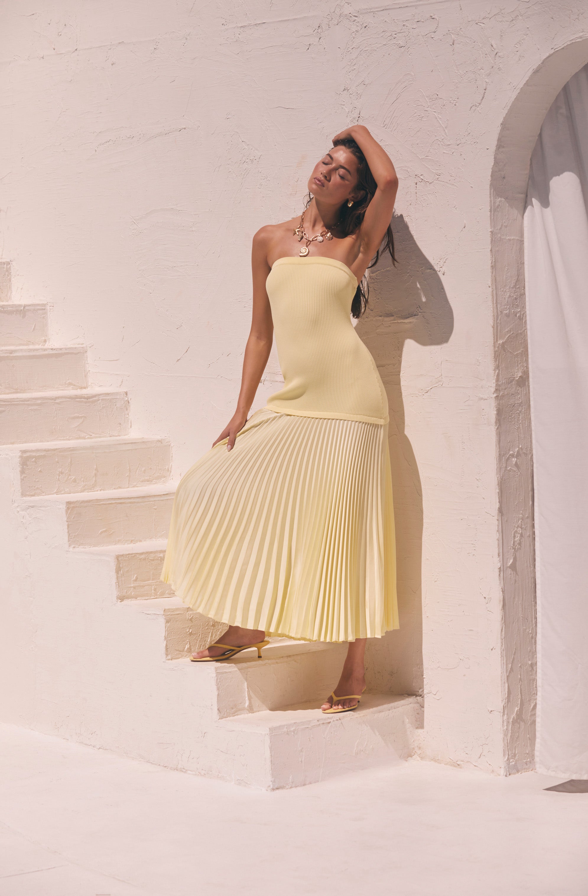 Woman wearing a strapless yellow dress with a fitted top and pleated skirt.