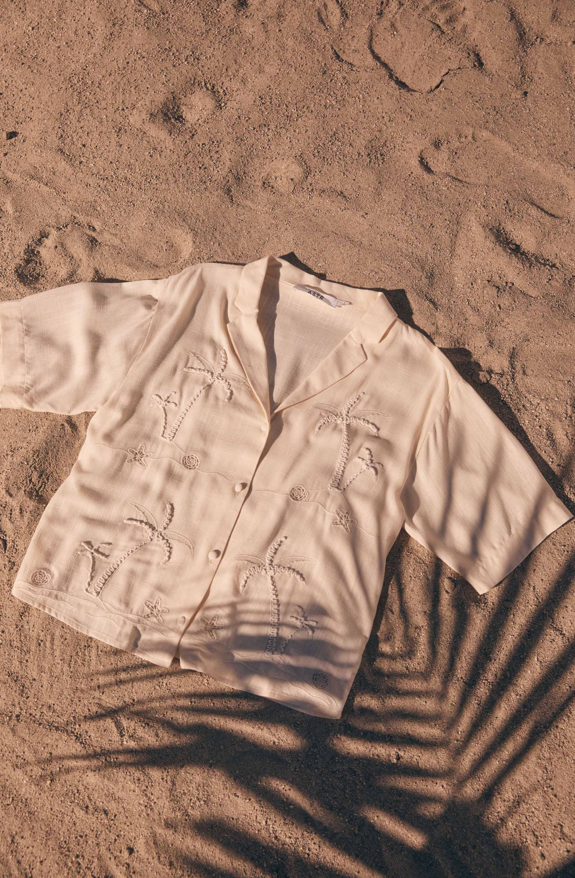 Light-colored short-sleeve button-up shirt with embroidered palm trees.