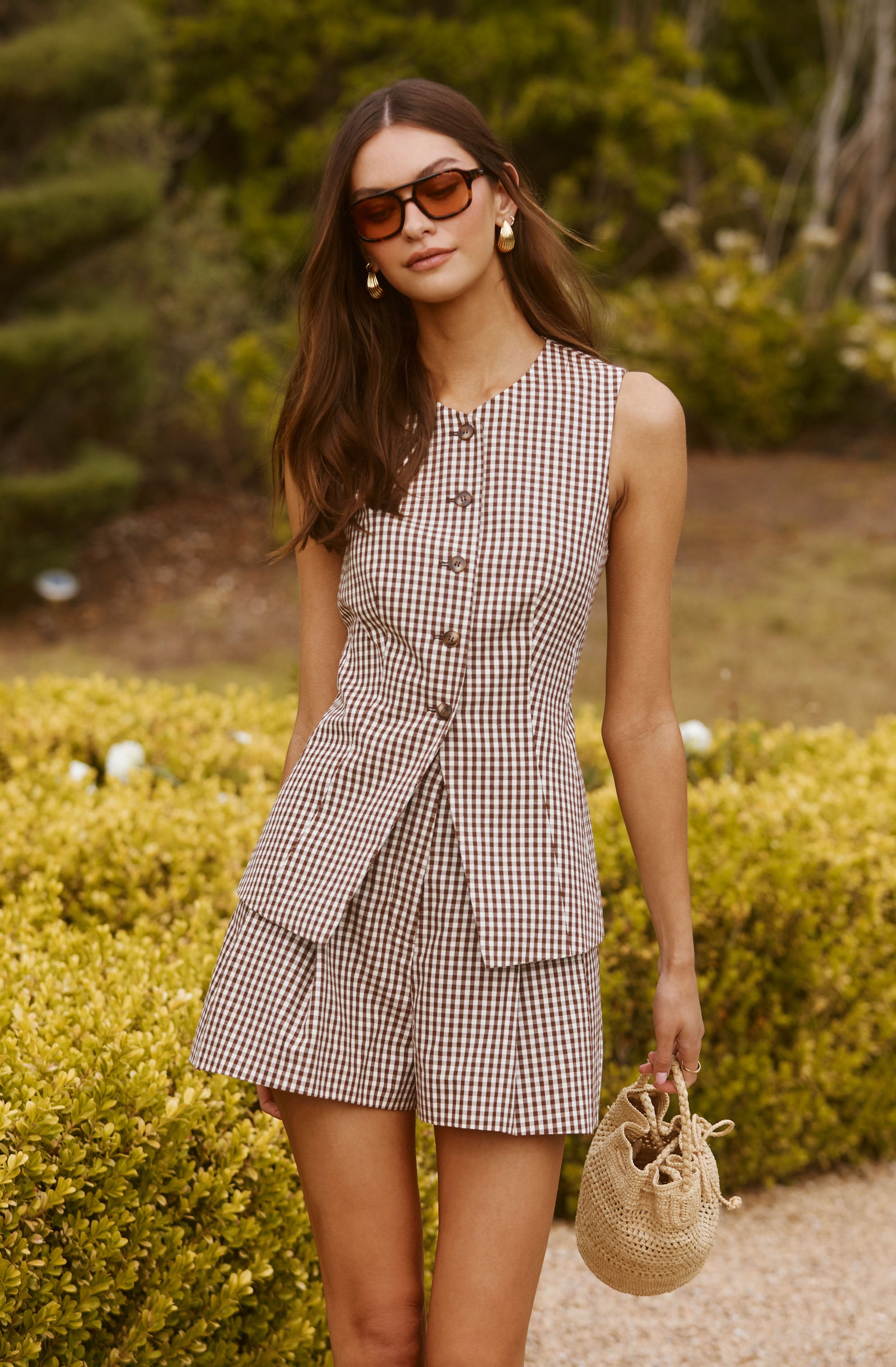 Woman wearing a sleeveless, button-up, checkered top with matching shorts and sunglasses.