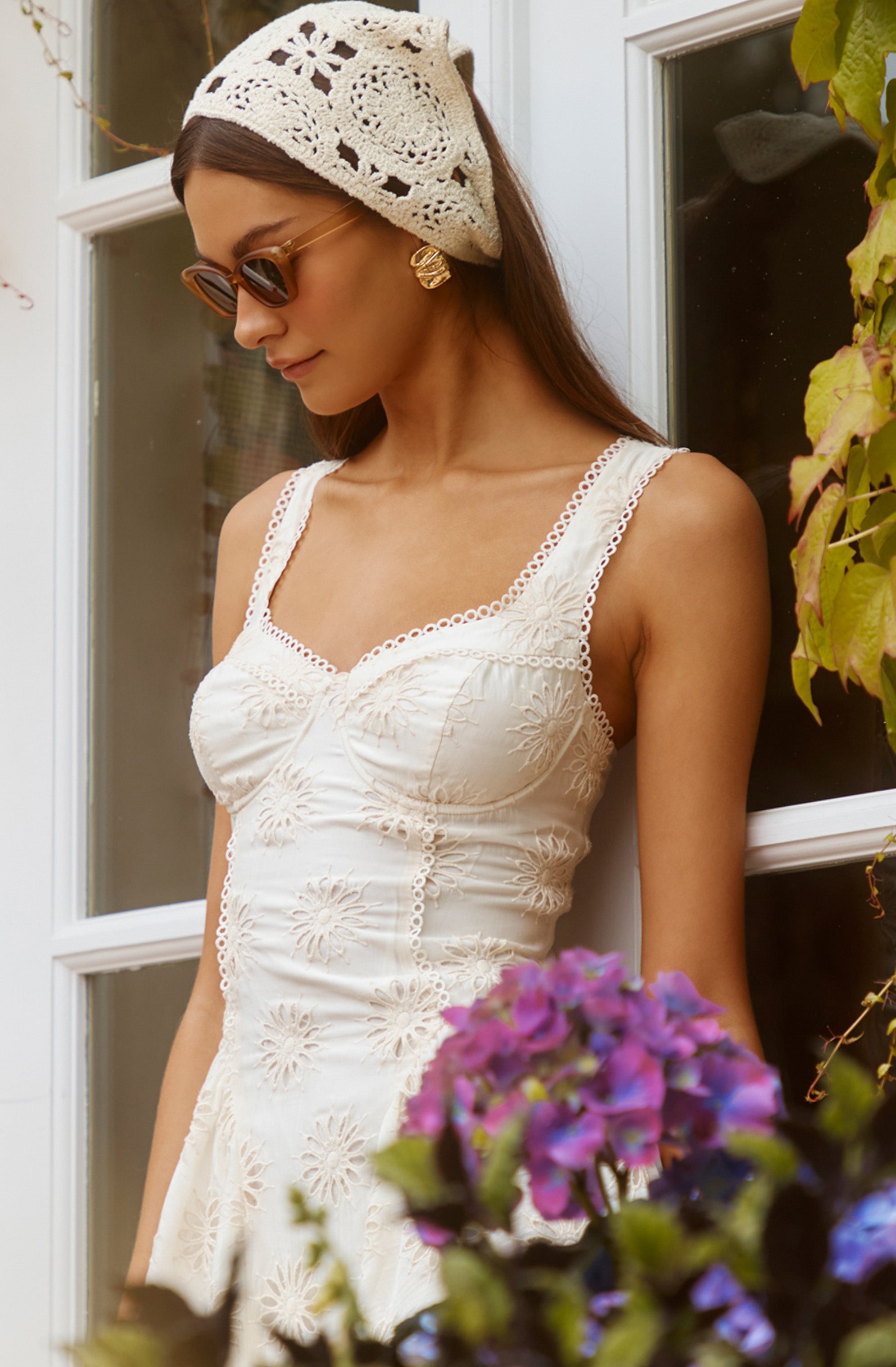 Woman wearing a white embroidered sleeveless dress, beige crochet hat, and sunglasses.