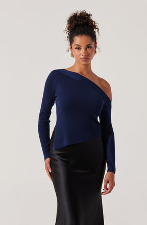 The woman is wearing a dark blue, off-the-shoulder, ribbed knit sweater with long sleeves. She is also dressed in a high-waisted, black, satin or leather-like skirt that falls below the knees.