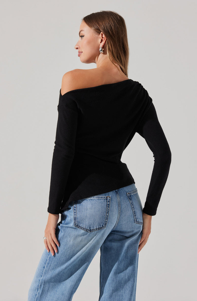 A woman wearing a black off-the-shoulder long-sleeve top paired with light blue, high-waisted, loose-fitting jeans.