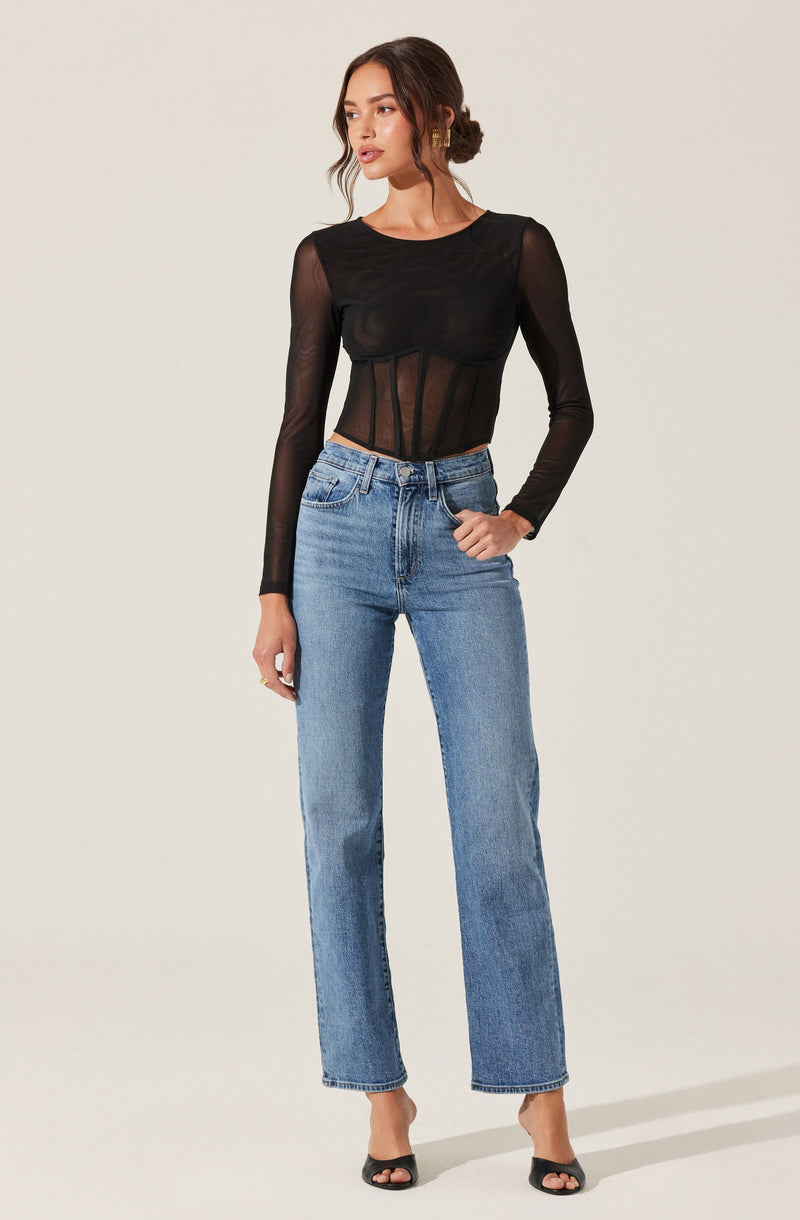 A woman is wearing a fitted black sheer long-sleeve top with a round neckline and vertical stripe details on the front. She is also wearing high-waisted, straight-leg blue jeans with minimal distressing and black open-toe heels.