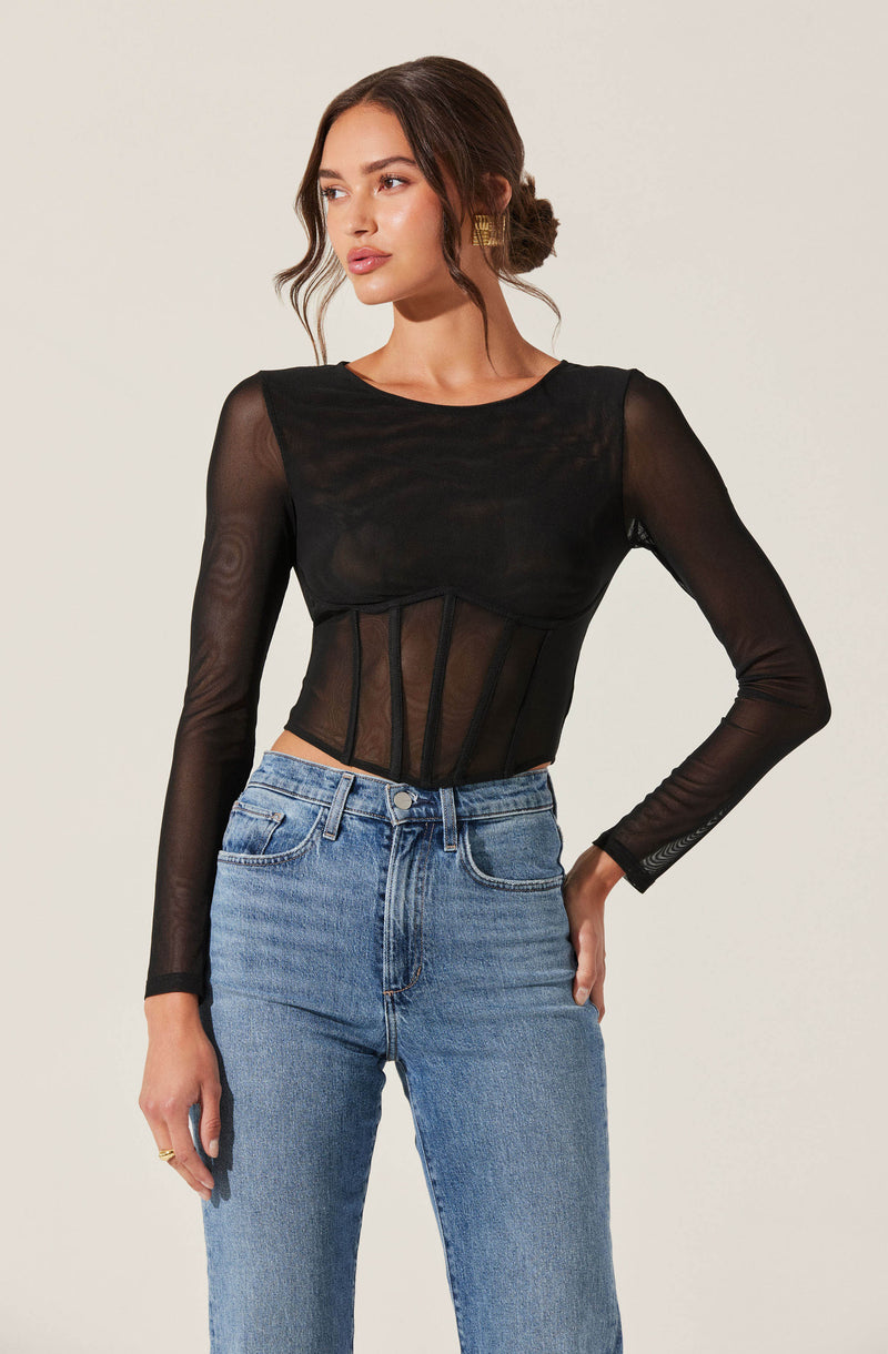 A woman is wearing a black, long-sleeved, semi-sheer top with a round neckline. The top features mesh fabric on the sleeves and torso with vertical seam details that create a corset-like appearance. She pairs it with high-waisted, light blue jeans with a classic five-pocket design.
