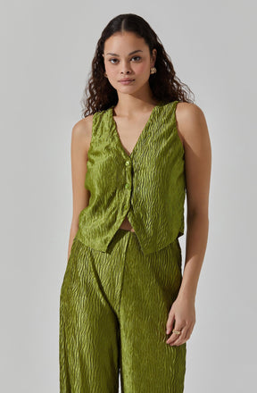 A woman is wearing a sleeveless, lime green outfit made of textured, shiny fabric with a wave-like pattern. The top is a vest style with a V-neck and buttons down the front, paired with matching wide-leg pants featuring the same textured design.