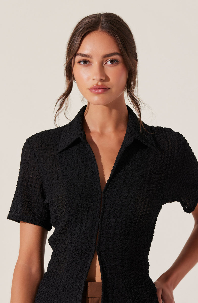 A woman wearing a black textured short-sleeve button-up shirt with a collar. The shirt has a slightly open front, revealing her midriff.
