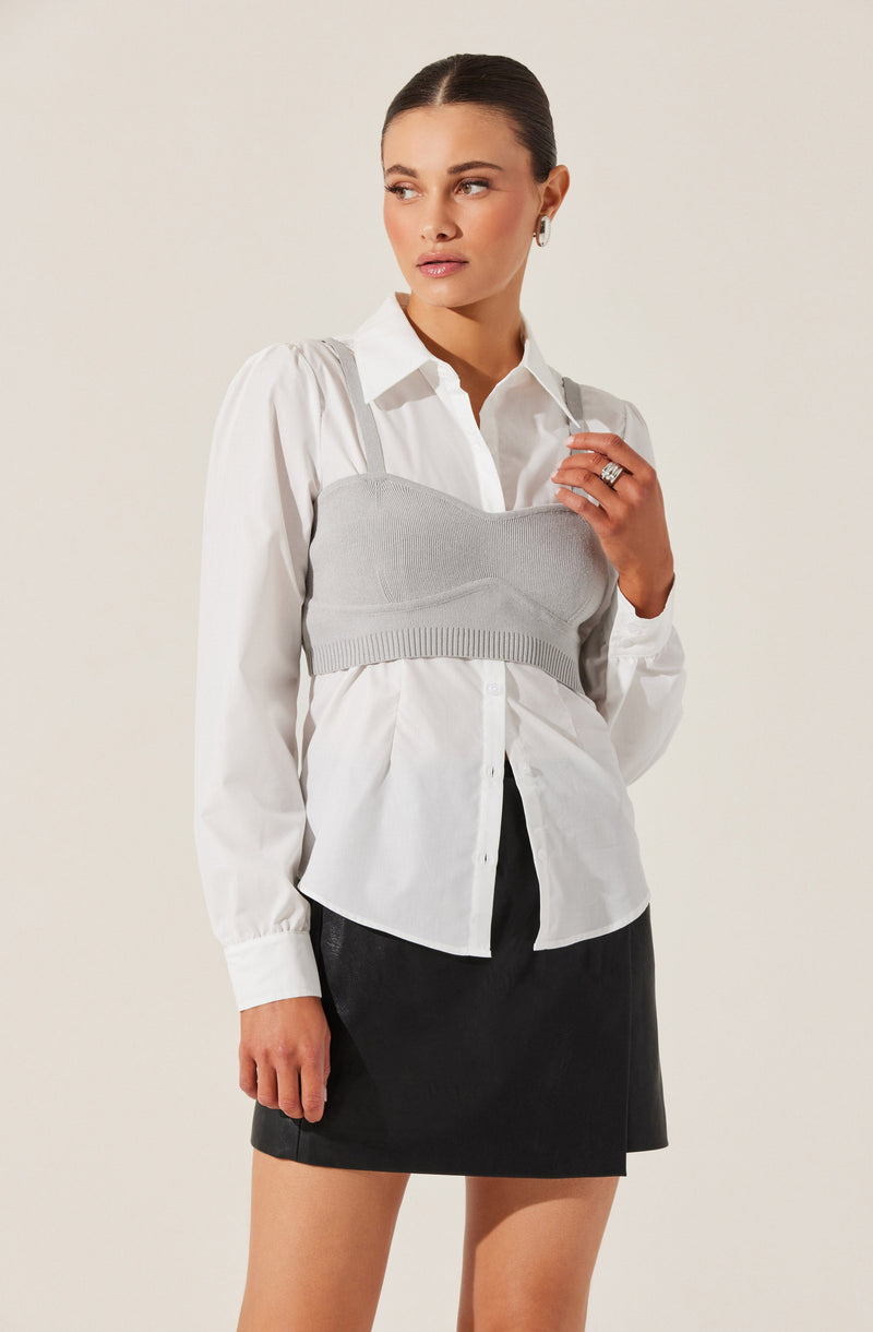 A woman is wearing a white button-up shirt with long sleeves and a collar, layered underneath a light gray, sleeveless, cropped knit tank top with thin shoulder straps. She is also wearing a black skirt.