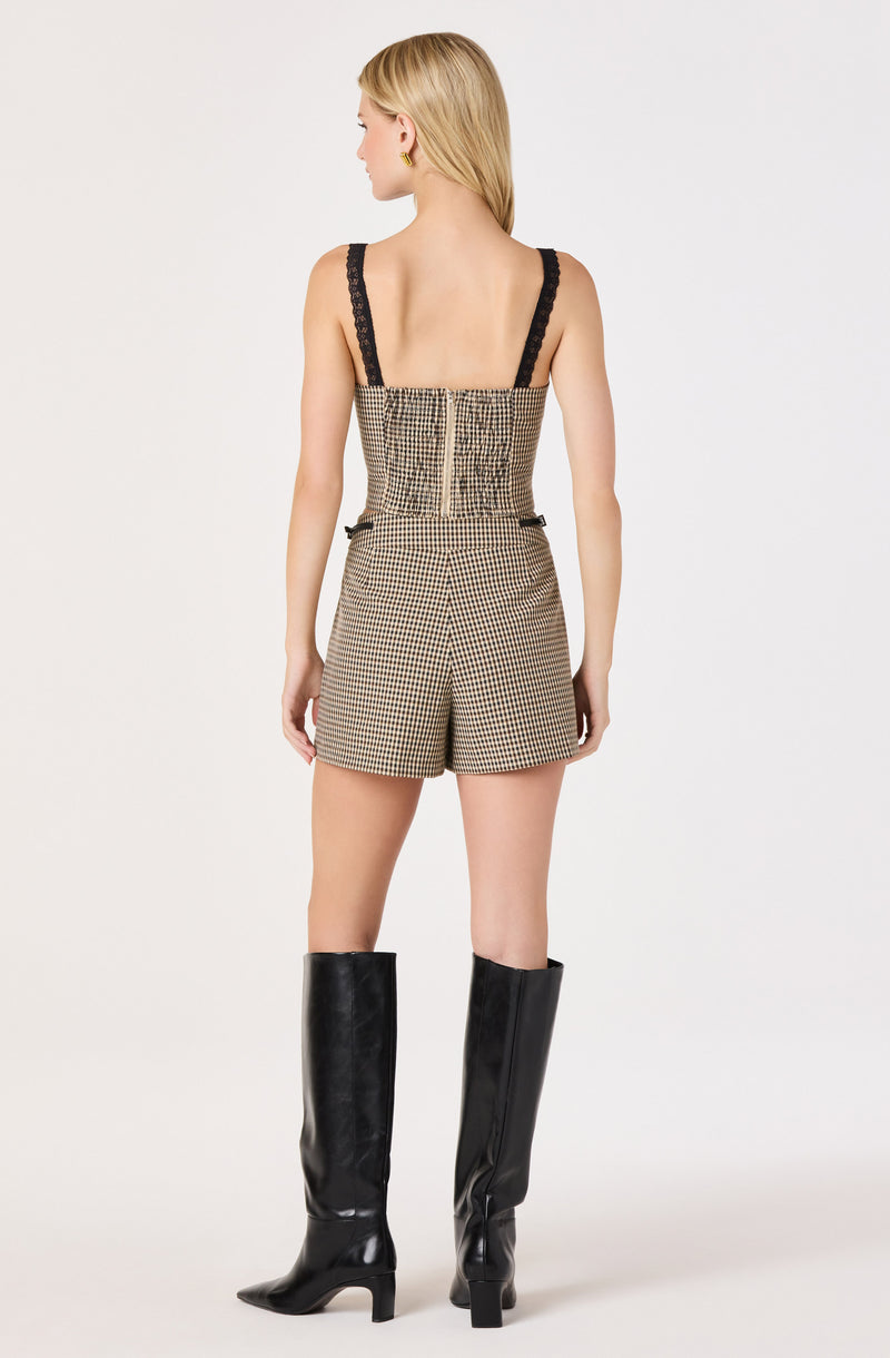 Woman wears a sleeveless houndstooth romper with black lace straps and gold zipper, paired with tall black boots.