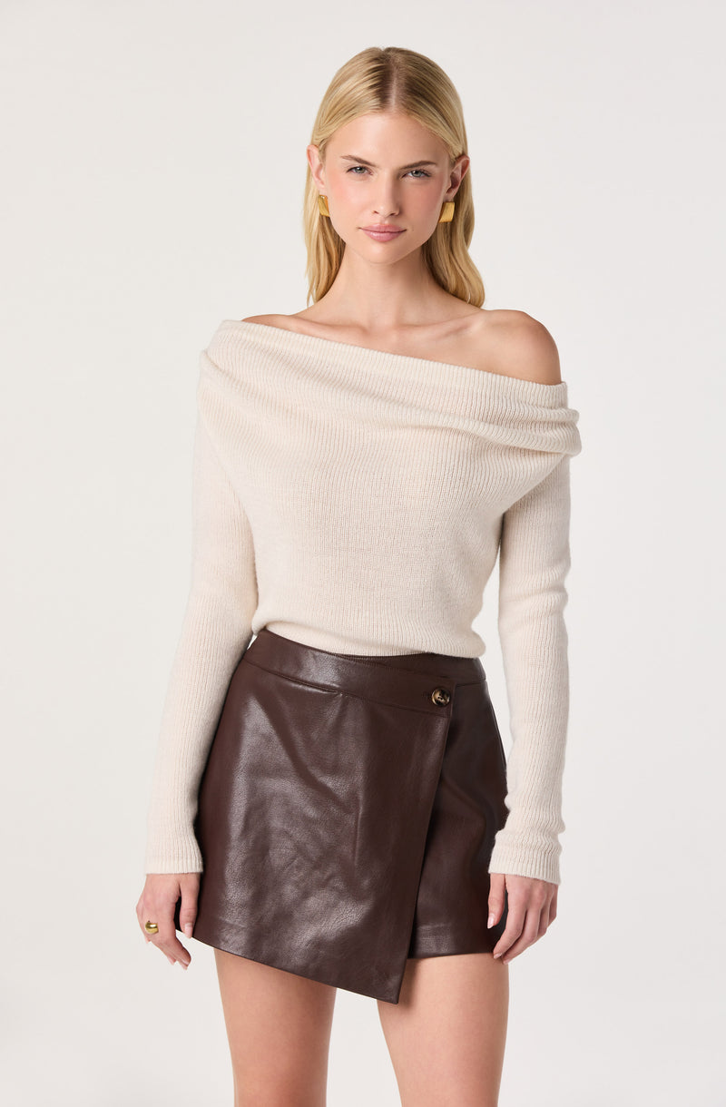 Woman wearing an off-the-shoulder cream knit sweater and a high-waisted brown leather skirt.