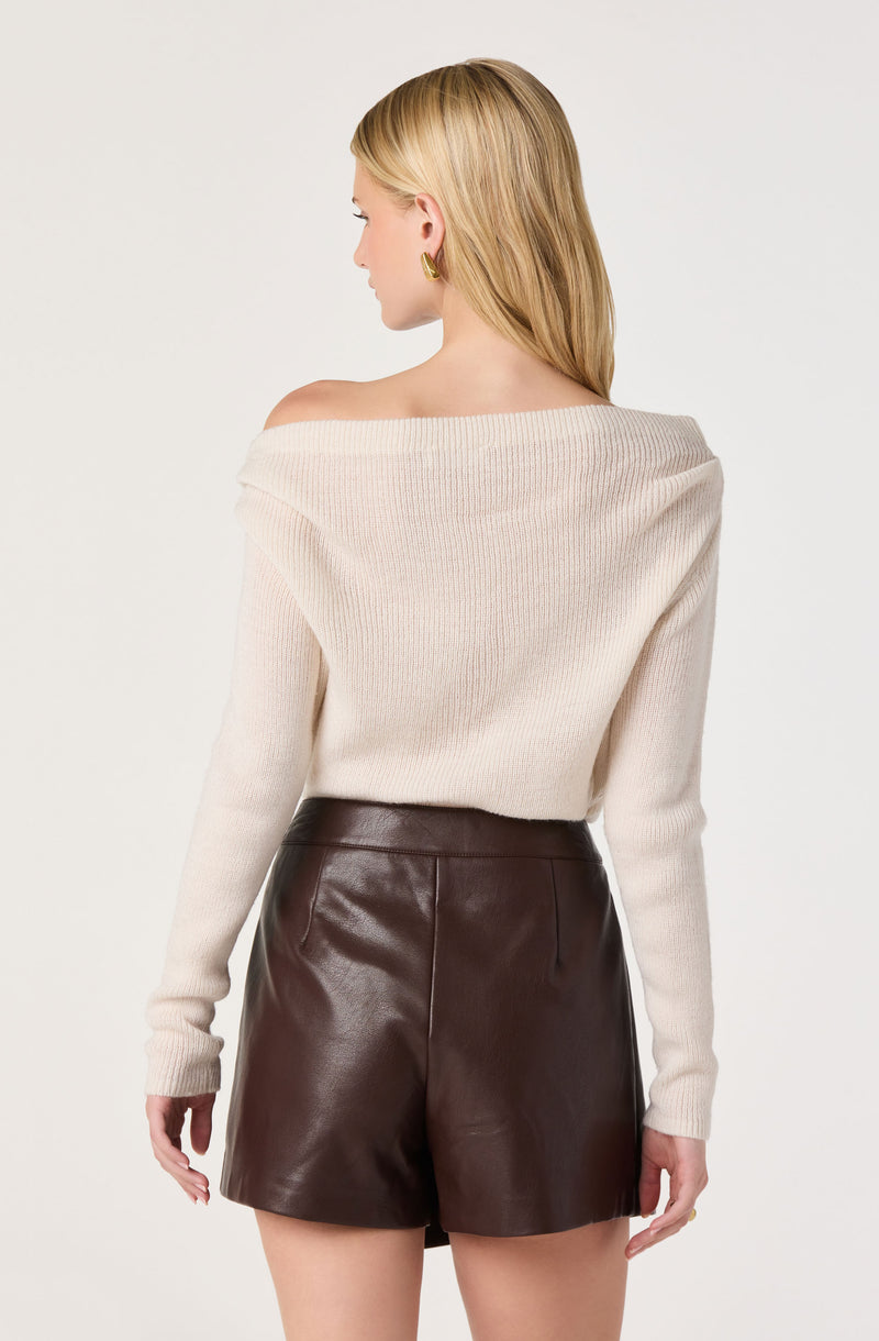 Woman wearing a cream off-the-shoulder sweater and high-waisted dark brown leather shorts.