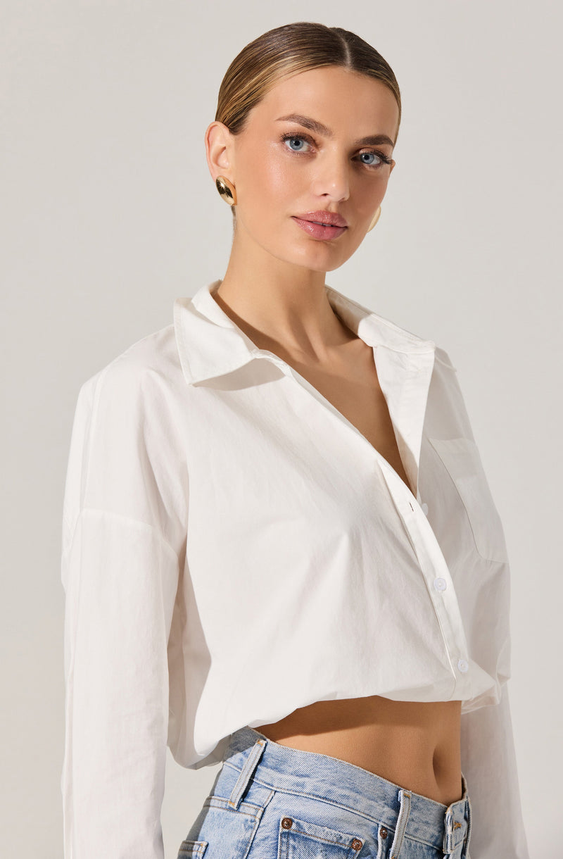 A woman is wearing a loose-fitting, long-sleeved white button-up shirt with a classic collar. The shirt is partially unbuttoned at the top, revealing her neckline. She is also wearing light blue high-waisted denim jeans.