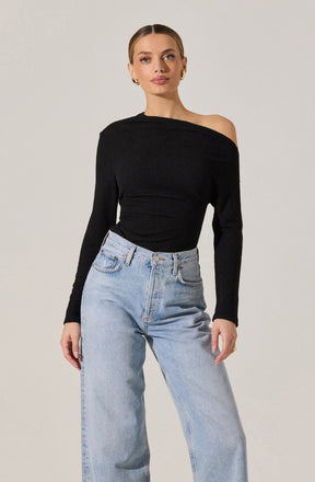 A woman is wearing a black, long-sleeved, off-the-shoulder top with a textured fabric, paired with high-waisted, light-wash jeans.