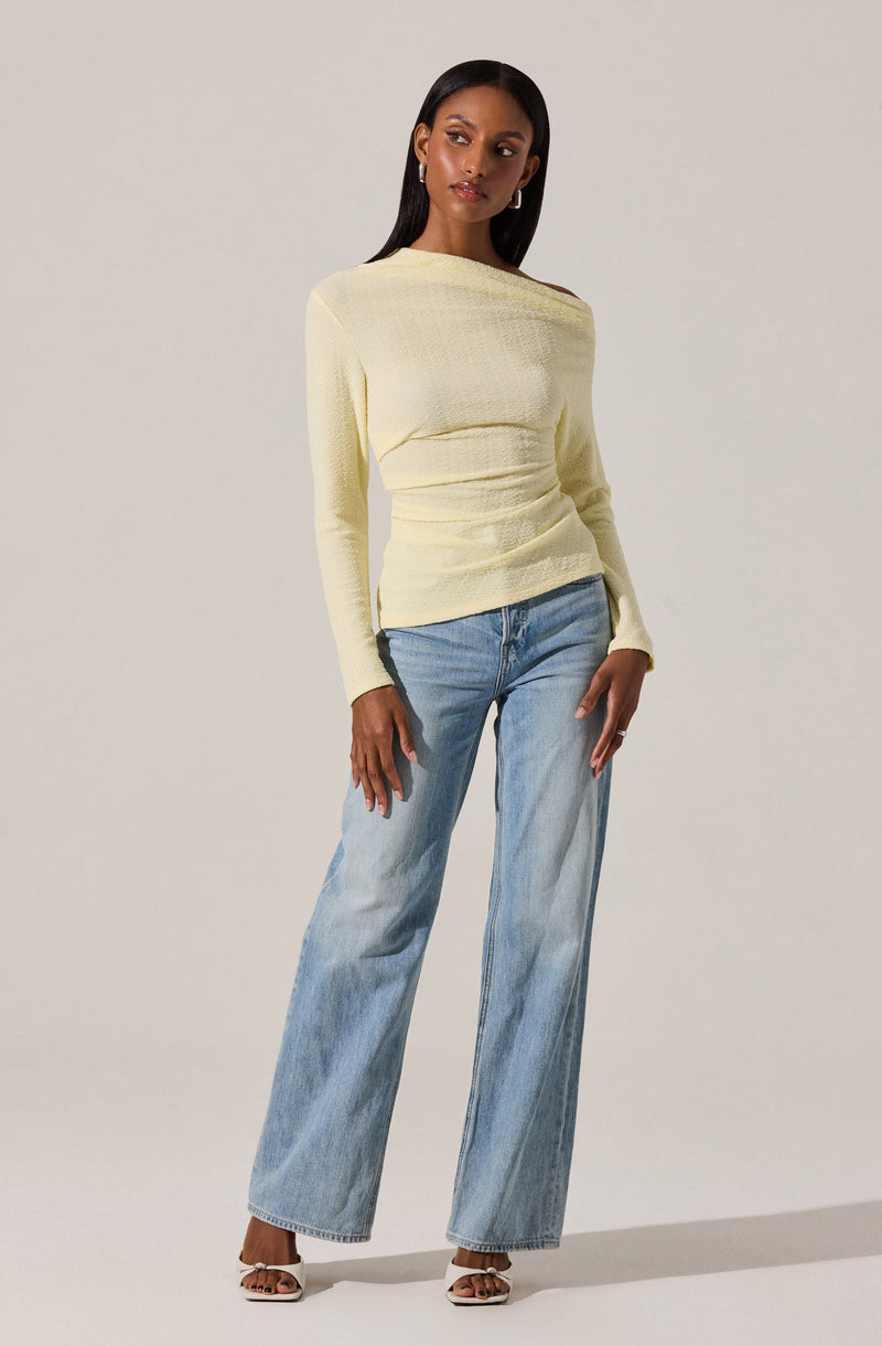 A woman is wearing a long-sleeved, light yellow top that has a textured, slightly shiny fabric. She pairs it with light blue, high-waisted, wide-leg jeans that have a relaxed fit. The outfit is completed with open-toe shoes with thin straps.
