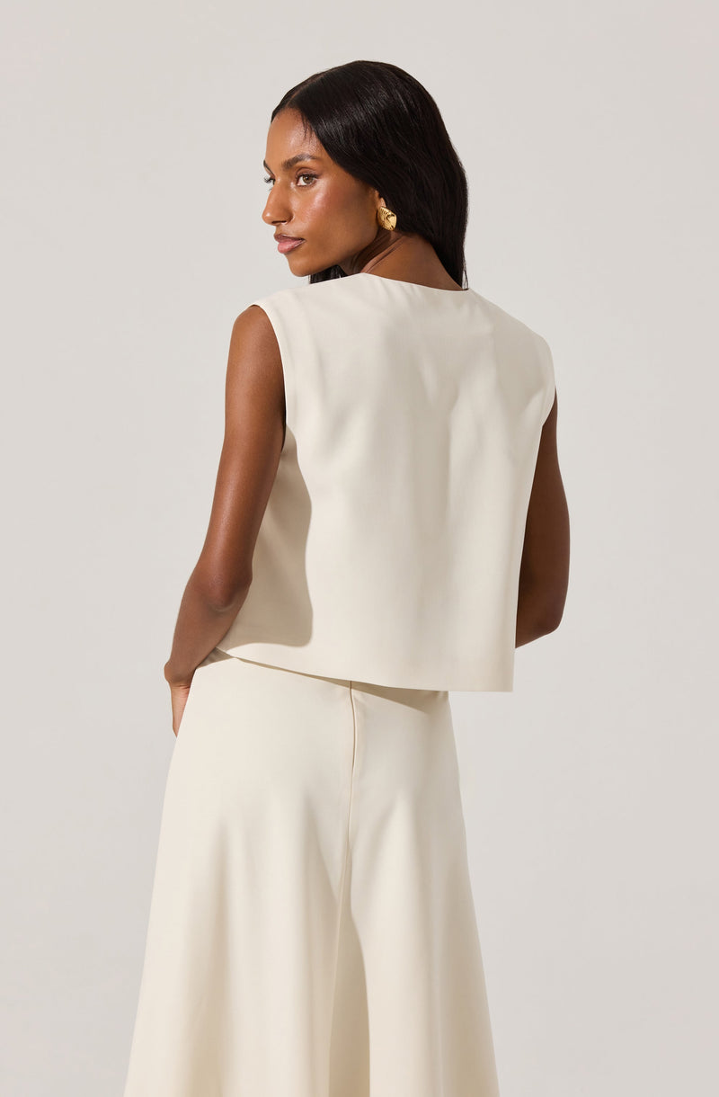 A woman is wearing a sleeveless, cream-colored top with padded shoulders that has a boxy fit, paired with matching wide-leg, high-waisted trousers. The outfit is minimalist and elegant, with no visible patterns or embellishments.