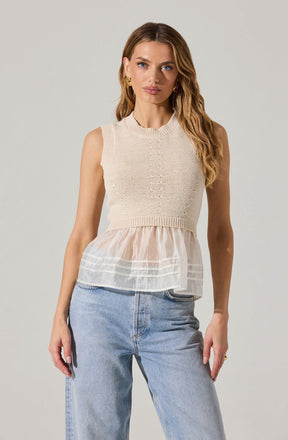 A woman is wearing a sleeveless, cream-colored knit top with a round neckline featuring a subtle ribbed pattern on the hem and armholes. The top has a layered design with a sheer, lightweight fabric extending below the knit section, creating a flowy, ruffled appearance with horizontal white stripes. She is also wearing light-wash, high-waisted jeans with a relaxed fit.