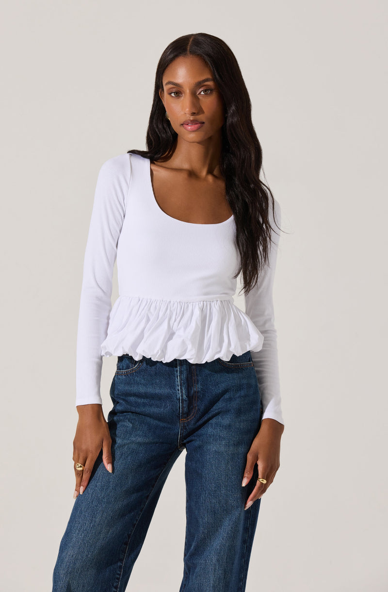 A woman is wearing a white, long-sleeved top with a scoop neckline and a ruffled, peplum-style hem. She pairs it with high-waisted, dark blue jeans.