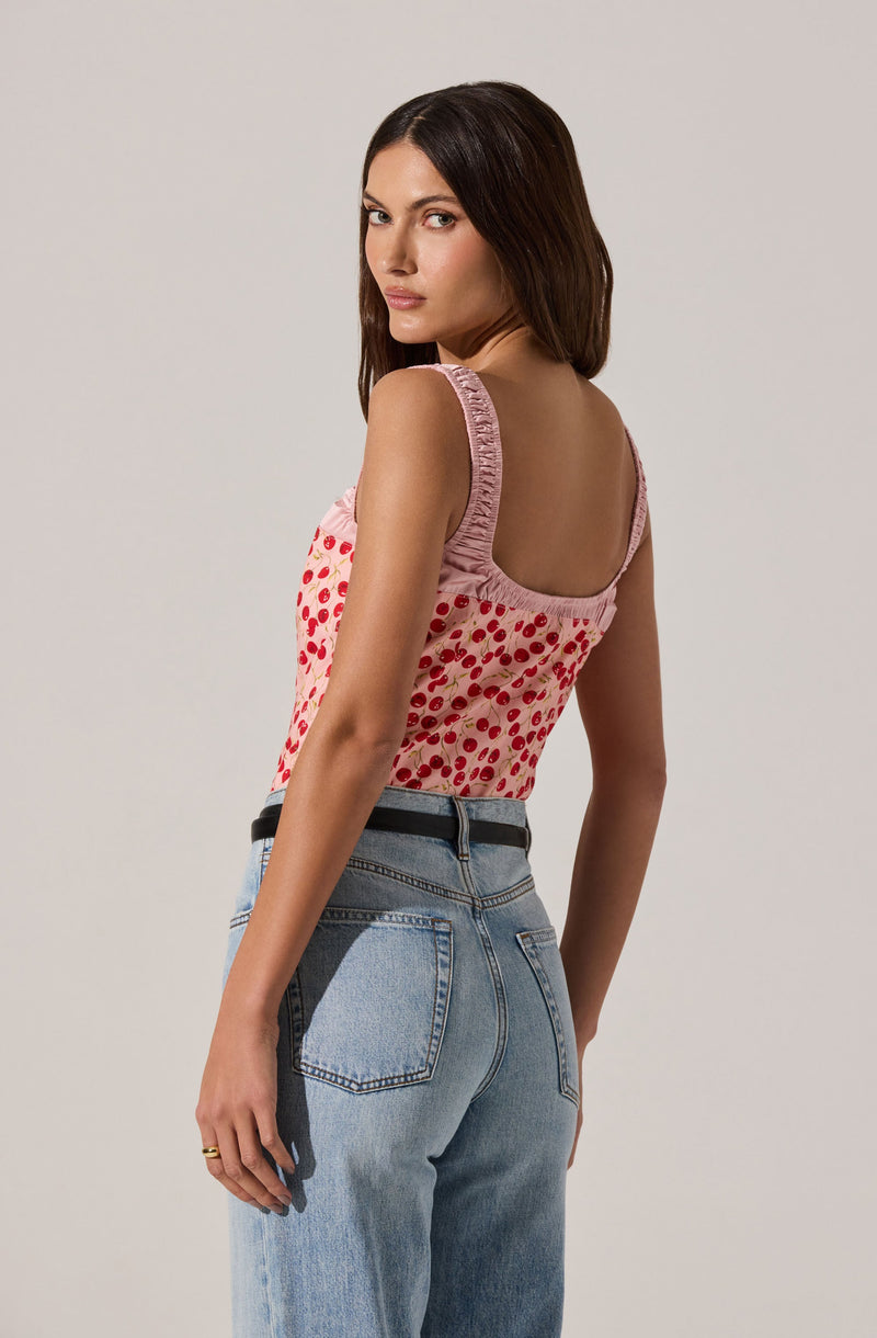 A woman is wearing a sleeveless top with pink ruffled shoulder straps and a pink and red polka dot pattern. She is also wearing high-waisted, light-wash denim jeans with a black belt.