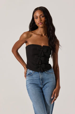 A woman is wearing a strapless black top with decorative bows along the front and a pair of light blue high-waisted jeans.