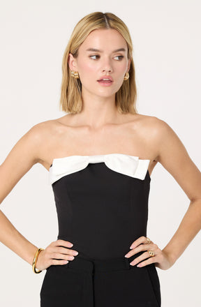 The woman is wearing a strapless black top with a large white bow detail across the chest.