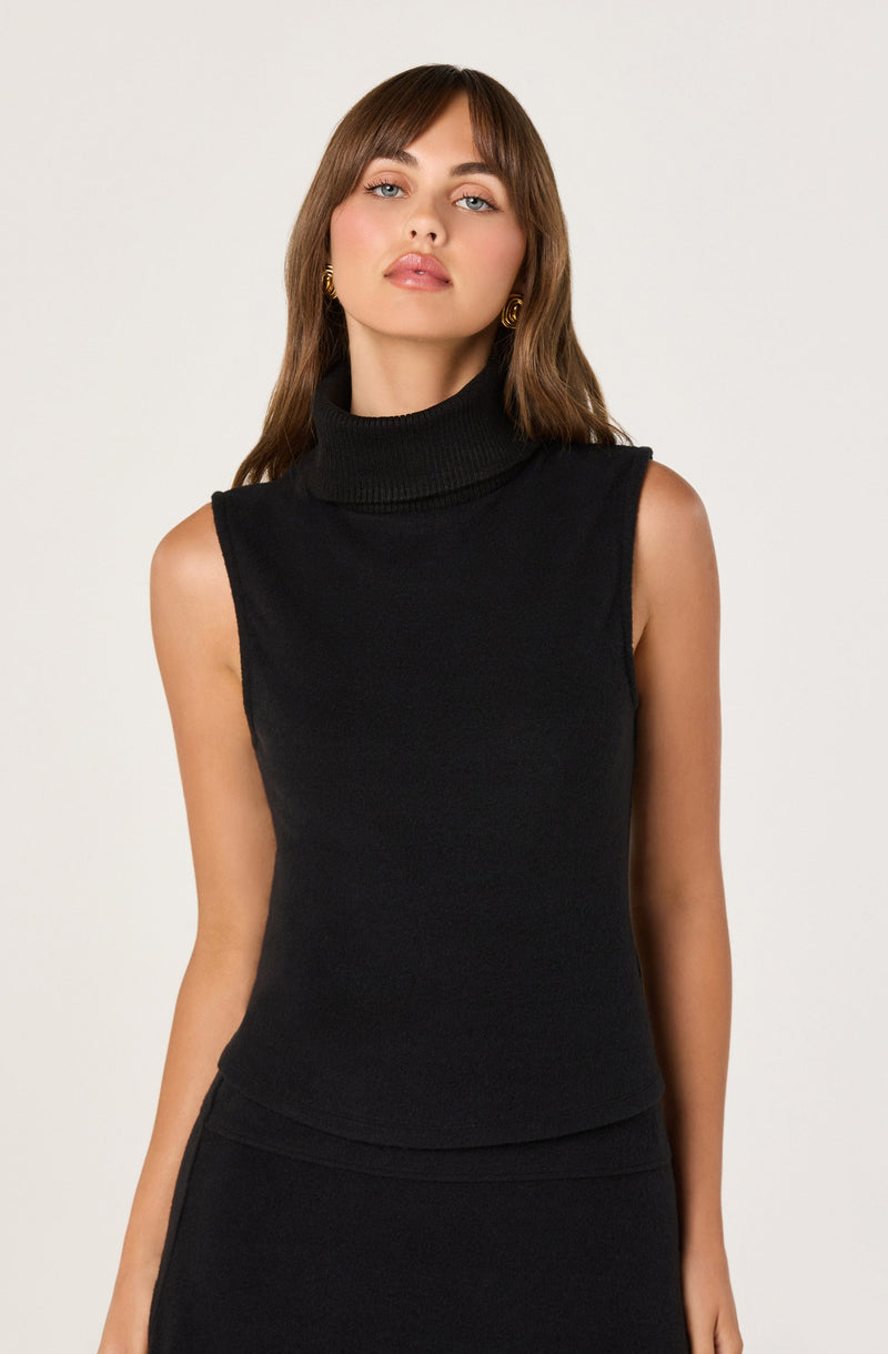 A woman is wearing a sleeveless black turtleneck top made of a ribbed knit fabric. She has paired it with a matching black skirt. The outfit is simple, elegant, and form-fitting.