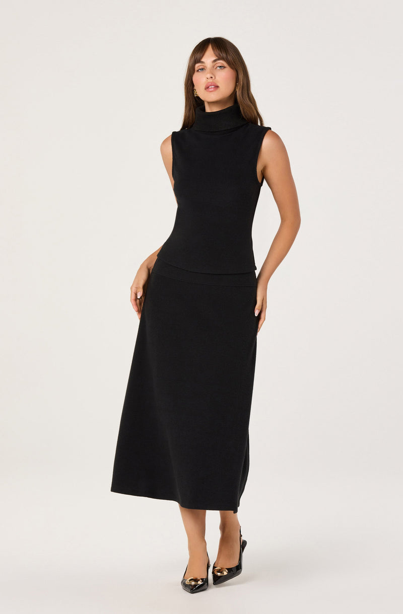 A woman is wearing a sleeveless black turtleneck top paired with a long black skirt. She has on black high heels with metallic accents at the toes.