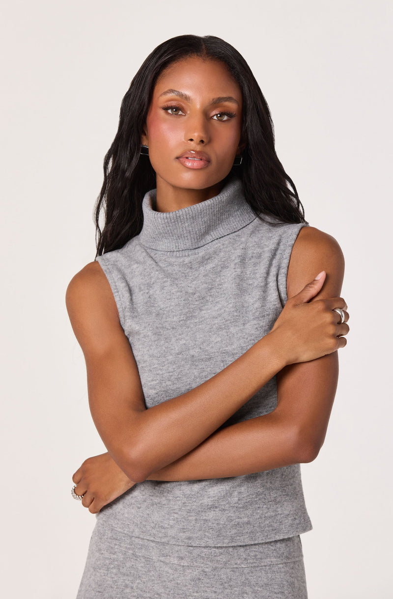 A woman is wearing a sleeveless, light gray turtleneck top made of a soft, knit fabric.