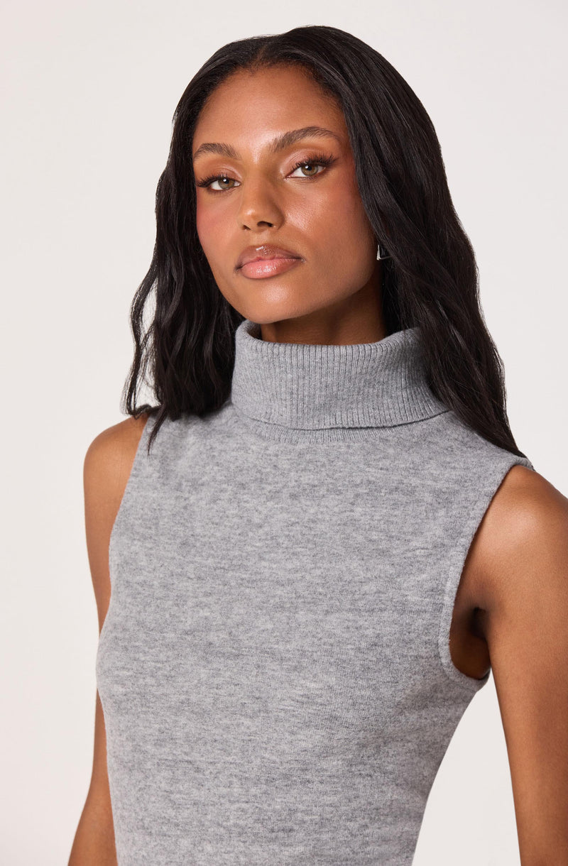 A woman is wearing a sleeveless, grey turtleneck top. The top has a fitted style and appears to be made of a soft, knit fabric.